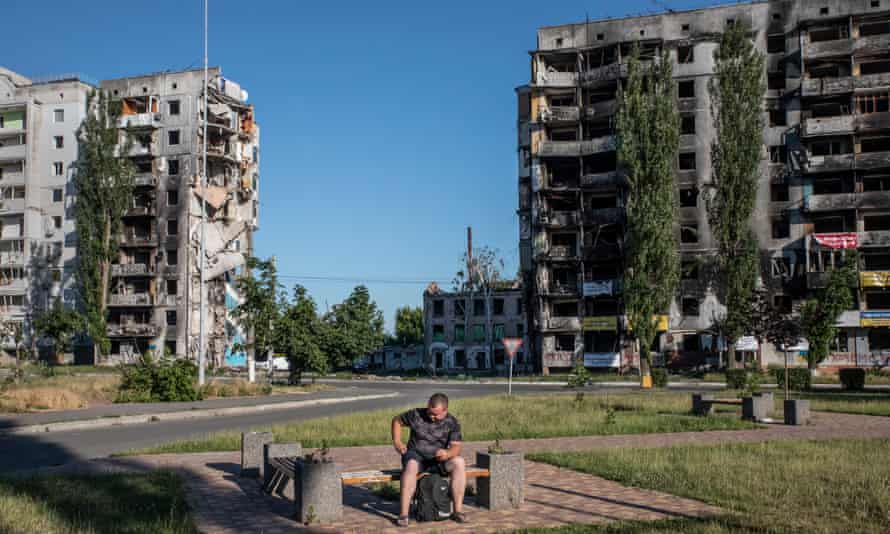 A man rests on a bench near destroyed residential buildings in the town of Borodyanka, July 2022