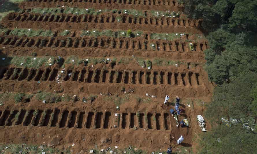 Workers in protective gear bury a person alongside rows of freshly dug graves at the Vila Formosa cemetery in Sao Paulo, Brazil