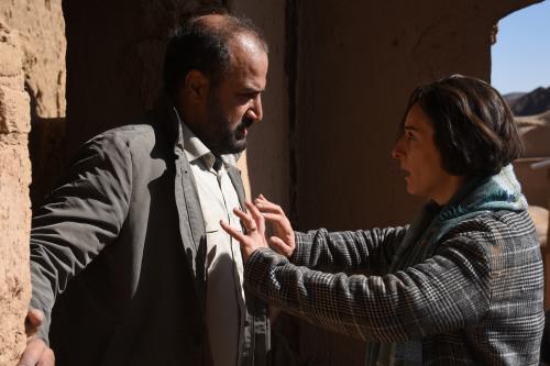 actor Soheila Golestani about to push actor Missagh Zareh in the chest – they’re standing outside in the sun beside a stone building – in The Seed of the Sacred Fig.