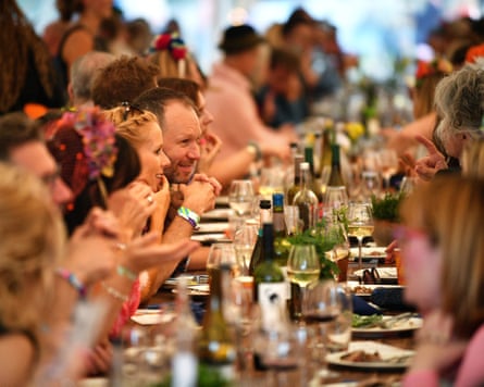 Festivalgoers sit at a long dining table with bottles and glasses of wine and plates of food at Wilderness festival.