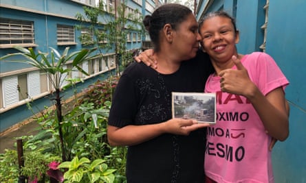 Maria Cleudimar da Silva and her daughter, on the balcony of their flat in São Paulo; she holds a photo of the wooden shack she lived in before the government built her current home