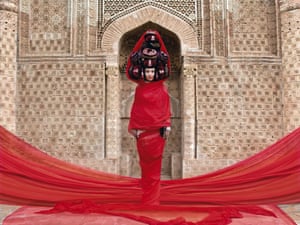 A model is enveloped in red fabric and adorned with several traditionally male headdresses