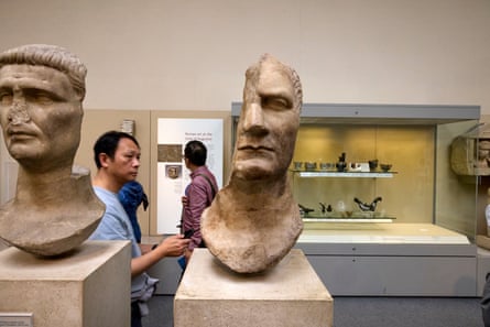 Two stone Roman busts, one cast in half by what must have a huge sword; a museum visitor passes by.