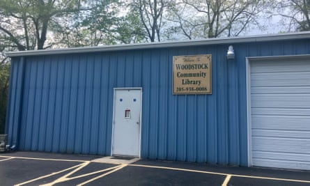 A blue-painted storage container with a white door and white garage door, and a lacquered wooden sign that says ‘Woodstock Community Library’.