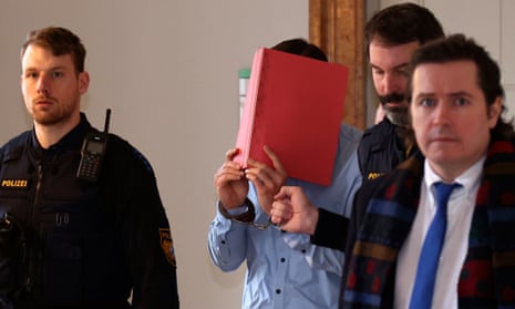 The defendant holds a book over his face as he is led into court