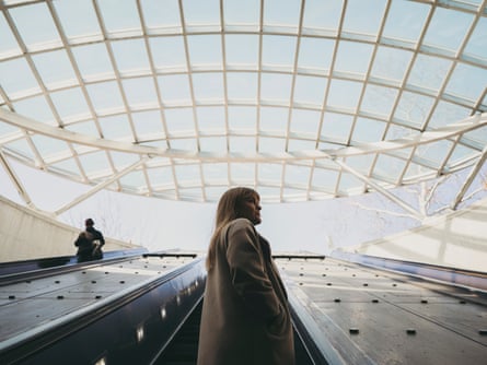 A woman takes an escalator up underneath a grid-patterned ceiling.
