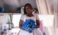 Memory poses inside a caravan wearing a wedding dress with lace bodice and holding a blue bouquet of flowers