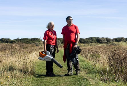 A woman and a man wearing red T-shirts, the woman holding a leaf blower