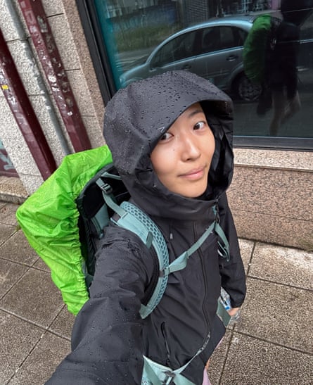 woman in rain jacket walks with backpack with green rain cover