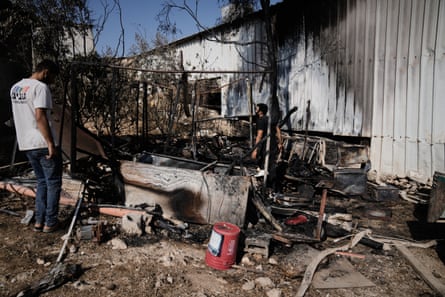 A man stands next to a burned and destroyed agricultural outhouse.
