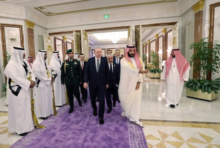 Erdoğan walks along a purple carpet with his entourage as he is led through a corridor by Mohammed bin Salman