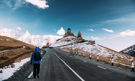 A tourist backpacker climbing to the hilltop Gergeti Trinity church in the Kazbegi mountains, Georgia.