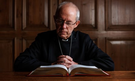 Justin Welby in his clerical collar sitting in a wood panelled room reading a bound Bible