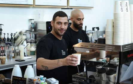 A man in a black T-shirt holds a cup behind the counter in a coffee shop.