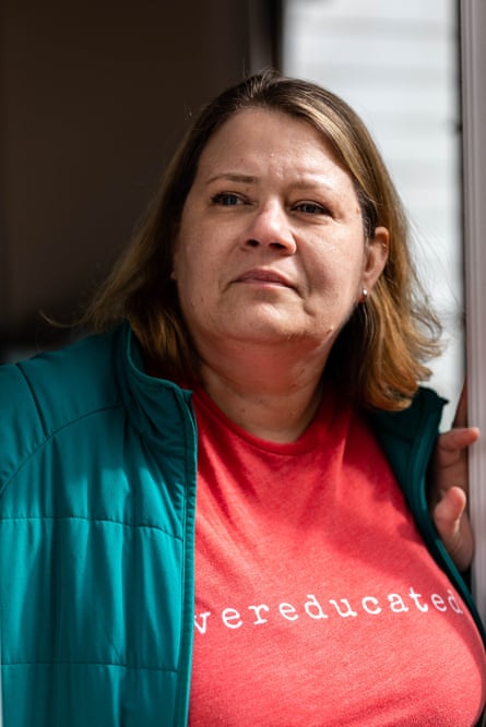 A person in a red shirt that says “overeducated” stands near a window