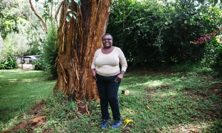 A woman in black jeans and a white top standing in a garden by a tree