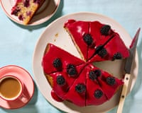 A cake with a red topping and blackberries on top, on a plaace with other plates and crockery nearby