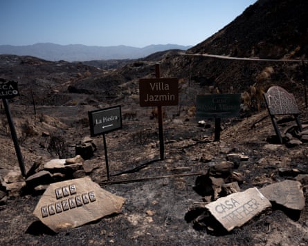Signs to Villa Jazmin and other homes gathered in front of a charred black valley landscape