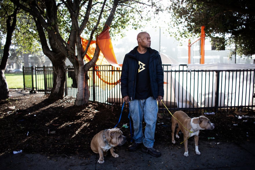 Eric Clark with his dogs. Behind him are the tents of other homeless people in West Oakland.