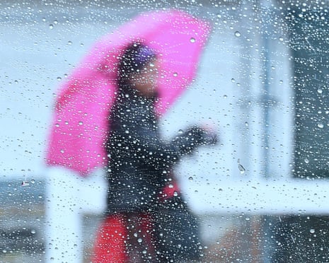 Raindrops are seen on a vehicle’s window as a woman walks by using an umbrella.