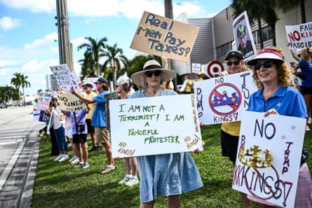people hold signs that read ‘real men pay taxes’ ‘I am not a terrorist. I am a peaceful protester’ and ‘no kings’