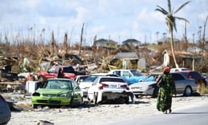 A woman walks by destroyed cars in the Mudd neighborhood in Marsh Harbour, Great Abaco, on 7 September 2019, in the aftermath of Hurricane Dorian.