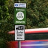 A Ulez sign with a blur of passing traffic including a London bus behind it