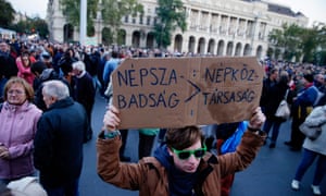 A demonstrator holds a placard reading, ‘Nepszabadsag, People’s Republic’ as crowds gather in front of the Parliament building in Budapest to show their support of the Hungarian political daily