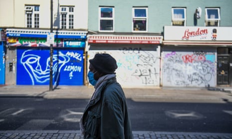 A woman wearing a mask walks along an empty Camden High Street in London.
