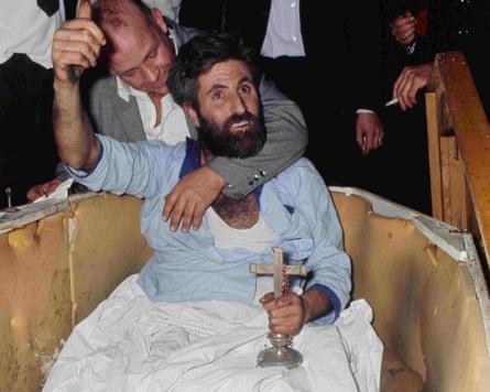 Mick Meaney lying in the coffin holding a crucifix gives the thumbs up as his manager embraces him.