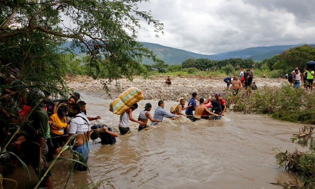 Line of migrants use a rope to cross waist-deep border river