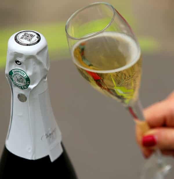 Someone holds a glass of champagne next to the bottle