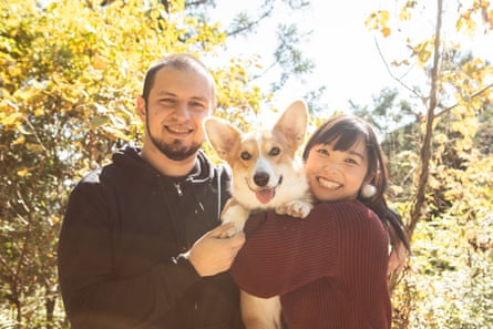 A couple in the autumn sunshine holding their Corgi dog