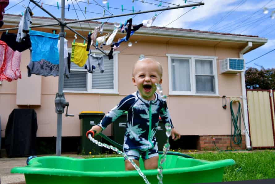 A toddler cools off by playing with a garden hose in a Sydney backyard.
