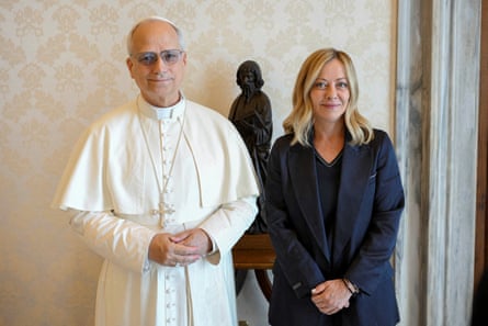 Pope Leo, in his traditional vestments, stands beside Giorgia Meloni who is wearing a dark blue blazer