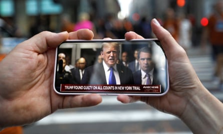 Two hands hold mobile phone turned sideways with image of Trump.