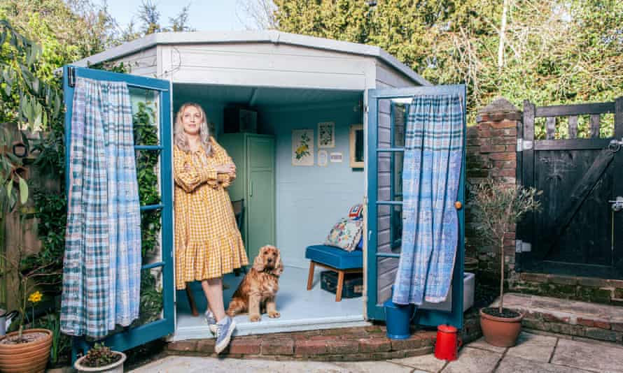 Camilla Perkins standing just inside her blue shed with kantha curtains hanging from the window doors