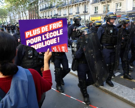 A protester holds a placard reading "More money for public schools" towards French CRS riot police who stand in position during a demonstration in Paris.