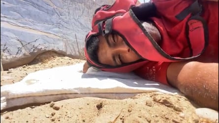 A man lying on sanding ground next to a rock