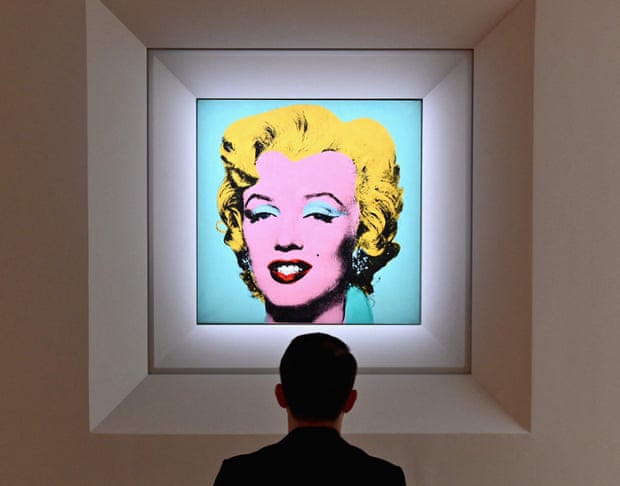 A man looks at Warhol’s vivid screenprint Shot Sage Blue Marilyn in a dim gallery