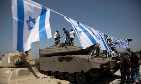 Israeli teenagers climb a tank decorated with flags