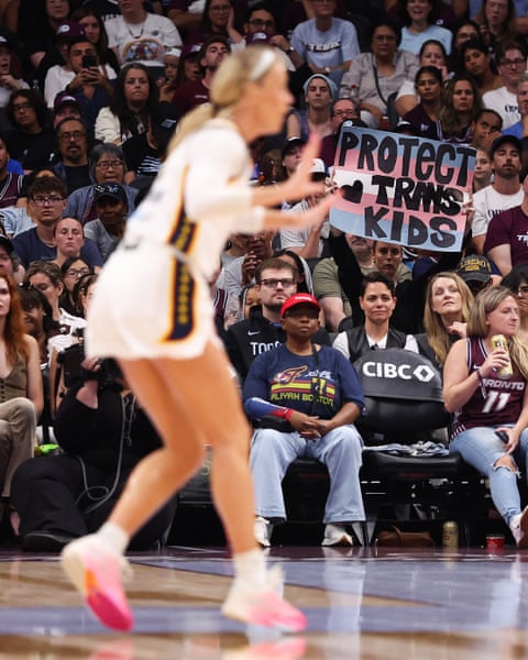 Sophie Cunningham on a basketball court as a fan holds a sign reading "Protect Trans Kids"