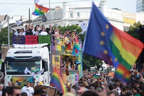 Dozens of people stand on a parade bus and line the streets in Hamburg with rainbow flags.