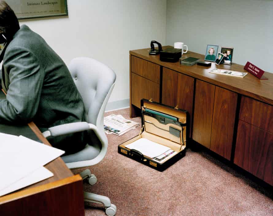 Man sitting at a desk, face out of shot, with his back to a sideboard with family photos on it
