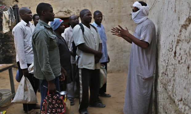 A smuggler (with covered face) talks to a group of men.