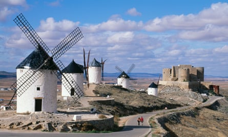 Windmills and castle overlooking the plains of Castilla La Mancha, Spain; image shows a couple walking together.