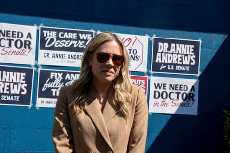 a woman stands in front of a wall with her campaign signs on it