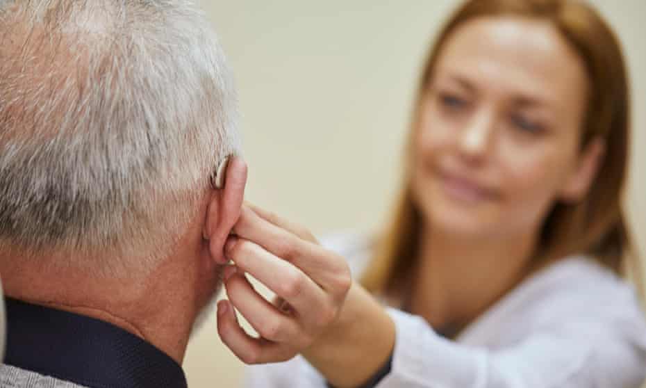 Female doctor applying hearing aid to senior man’s ear