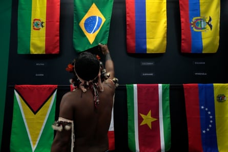 An Indigenous man stands before eight flags of Amazon countries, including Brazil