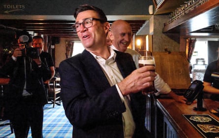 The UK prime minister, Andy Burnham, and the chancellor of the exchequer, John Healey, smile while being photographed in a pub.